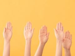 Mehrere Hände werden vor einem gelben Hintergrund gehoben.