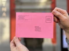 Eine Person hält einen pinken Wahlbrief in der Hand.